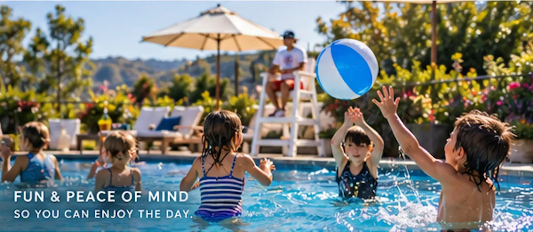 Children play with a beach ball in a pool while a lifeguard sits on a stand in the background.