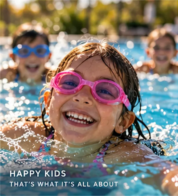 A smiling child in pink goggles swims in a pool with other children behind her.